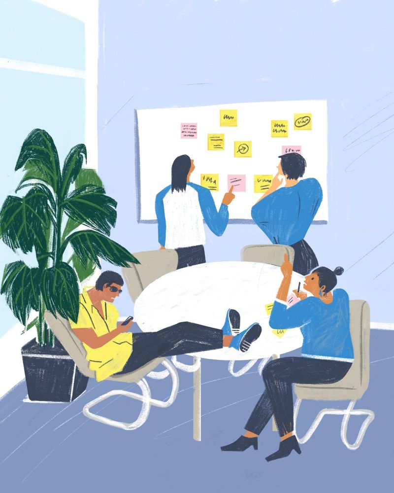 Vier Personen sitzen und stehen um ein Whiteboard herum. Eine hat die Füße auf dem Tisch, zwei kleben Post-its an.