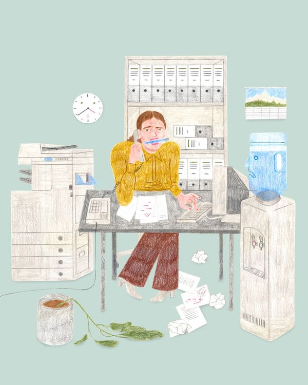 Eine Person sitzt ängstlich mit Stift im Mund und Telefonhörer am Ohr an einem überladenen Schreibtisch.