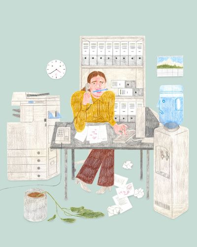 Eine Person sitzt ängstlich mit Stift im Mund und Telefonhörer am Ohr an einem überladenen Schreibtisch.